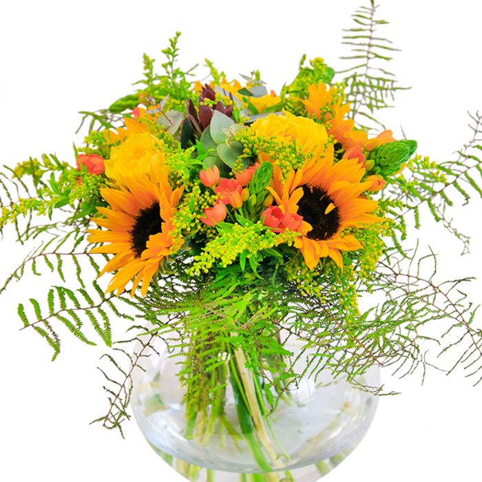 Radiating pure, sunlit joy, this abundant bouquet captures the vibrant energy of Garston in full bloom. Large, radiant sunflowers and sumptuous yellow roses push open their petals in warm, inviting layers, almost glowing with the brightness of a summer day in King George V Playing Fields. Contrasting this exuberance, clusters of gleaming red Hypericum berries nestle among rich foliage, popping against the soft matte of the petals and deep green leaves. The arrangement brims with movement and texture-a lively dance of cascading fern fronds, airy solidago, and slender green spikes, each detail thoughtfully placed by local Garston florists. Eucalyptus leaves, tinged with blue-green, lend a fresh, rustic accent, while smaller yellow blossoms add a gentle, golden highlight. The bouquet is cradled by a round, clear glass vase, allowing the fresh green stems to shine through like nature's artwork. Seen up close, the interplay of textures and colours feels tactile and joyous: suede-like sunflower faces, tightly furled rose petals, and leafy freshness combine in a tapestry that is both visually and emotionally uplifting. This is the perfect arrangement for birthdays, anniversaries, or any occasion where heartfelt celebration is called for in Garston-an everyday reminder of natural beauty and the spirit of community.