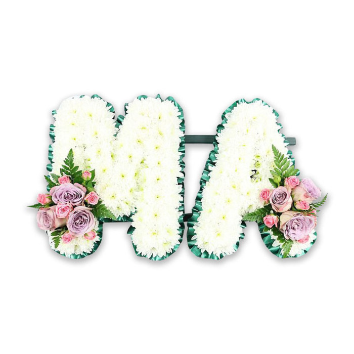 This photograph presents a dignified floral tribute spelling the capital letters MA, most likely created as a personalised remembrance for a mother or someone affectionately known as Mama in the Garston community. Both letters are formed from a sturdy frame, completely concealed beneath a dense layer of small white chrysanthemums. Each bloom sits tightly against its neighbour, forming a plush, cushion-like surface that looks almost like freshly fallen snow, yet with the gentle texture of overlapping petals. The contours of the M and the A are crisply defined by a deep, emerald-green satin ribbon, pleated into a soft ruffle that runs uninterrupted around every edge. This ribbon border lends polish and clarity to the lettering, while a dark green connecting bar at the base unites the two forms into one harmonious piece. At the base of the left leg of the M and the right leg of the A, matching accent sprays bring delicate colour and emotion. These feature soft lavender roses and pale pink roses, some fully open, others in half-blown stages, interwoven with dainty pink spray roses that add fine detail. A single arching fern frond in each cluster introduces a natural, feathery contrast to the compact petals, suggesting life and renewal amid sorrow. Photographed on a plain white background with even lighting, the tribute's clean lines, pastel shades, and fresh greenery are emphasised, making it easy to imagine this arrangement resting near a coffin, on a hearse, or at a crematorium service. It feels like a thoughtfully designed funeral letter tribute you might order for same-day delivery in and around Garston when you wish to express love, respect, and cherished memories in a simple but deeply personal way.