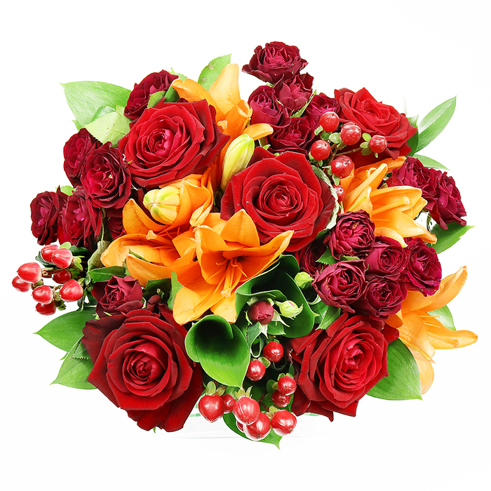 Captured from directly overhead against a pristine white background, this abundant floral circle presents a rich choreography of colour and form: several large, fully unfurled deep red roses anchor the design, each velvety petal layered to reveal delicate, romantic centres. Scattered among them, bold orange Asiatic lilies provide dramatic trumpet silhouettes-some blossoms open wide with stamens on display, others in mid-bloom or tight buds-so the composition feels alive and unfolding. Small, tightly petaled spray roses in dark burgundy create shadowed pockets of depth, their clustered geometry lending a luxurious textural counterpoint to the open roses. Glossy Hypericum berries sit like tiny garnets across the surface, catching the soft studio light and adding a festive, tactile punctuation. Generous swathes of green foliage-broad, glossy leaves such as ruscus or salal-peek through, offering cooling contrast and structural rhythm that keeps the warm palette grounded. The overall impression is opulent yet balanced: the bouquet's colours-rich reds, warm oranges and fresh greens-evoke late-summer and autumnal warmth, moments of celebration or intimate romance. If you imagine this arrangement on a white dining table in Garston village or brightening a mantel in a local home, you'll sense its ability to transform a space with texture, scent and colour. Meant for significant occasions like anniversaries, romantic surprises, or as a lush gift to express appreciation, this piece mirrors the thoughtful, hands-on approach typical of florists serving the Garston community.