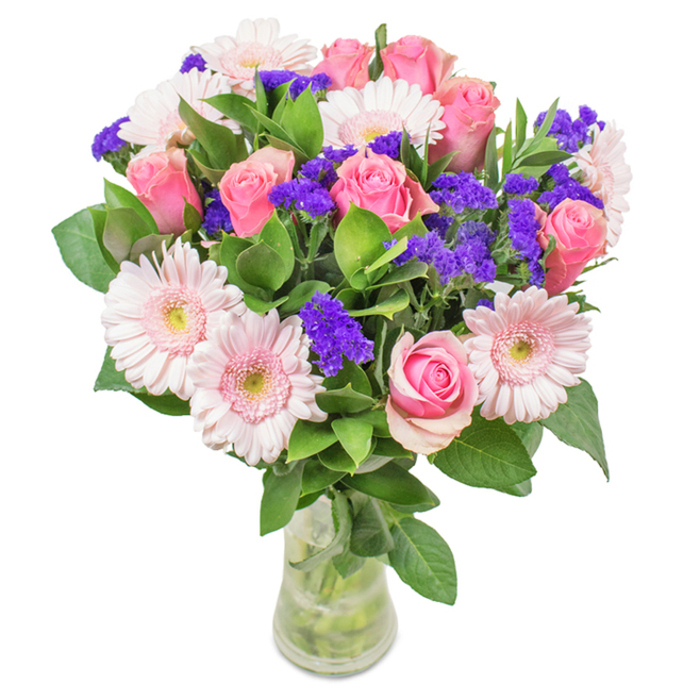 A fresh, elegant bouquet sits within a sparkling clear glass vase, its vibrant presence complemented by the pristine white backdrop often seen in Garston display windows. At its heart are roughly seven to nine soft-to-medium pink roses, some tightly furled and some just beginning to open, their spiral petals capturing classic beauty. These are perfectly balanced by about five to seven pale pink gerbera daisies, identifiable by their generous, round heads and cascading lighter petals, catching the softest daylight. Intertwined among the blooms, clusters of vivid purple statice or limonium provide striking texture and pockets of deeper tone. The base is designed with abundant, deep green foliage, which both grounds the palette and brings a sense of lushness akin to a stroll through Garston Nature Reserve. Stems and crisp water gleam through the vase, hinting at freshness and expert care-a hallmark of Garston's local florists. Ideal as a thoughtful birthday surprise, a Mother's Day tribute, or an understated yet meaningful home or office arrangement, this bouquet symbolizes joyful celebration and heartfelt sentiment, making it an appealing choice for flower delivery throughout Garston.