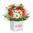 A fresh and uplifting floral bouquet, brimming with joy, graces a spotless white square gift bag-a vision easily recognized by Garston residents who favour thoughtful gestures and local surprises. The arrangement bursts with coral and peach carnations, their ruffled petals soft to the touch and rich in vibrant hues, interspersed with gleaming white daisies whose bright green-yellow centers seem to glow with life. Wispy clouds of baby's breath float among the principal blooms, casting an air of innocence and purity. Glimmers of unopened, purple-tinged buds quietly rest on one side, hinting at potential and new beginnings. Embracing it all, deep green, glossy leaves curl in an elegant arrangement, creating an inviting and natural base-echoing the community gardens and quiet green spaces of Garston. The bouquet's round and abundant shape, achieved by the careful artistry of local hands, is underscored by soft, even lighting that highlights every detail against a pure backdrop. Sturdy white handles beckon the recipient to lift and share the bouquet-delivering smiles for birthdays, thank-you gestures, or special surprises delivered by Garston's trusted floral experts. Each element is a tribute to freshness, impeccable care, and the simple joys found within Garston's friendly neighbourhoods.