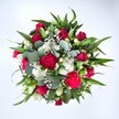 Viewed from directly above against a clean white background, this generous bouquet forms a perfect circle of colour, like a little garden gathered by hand somewhere off St Mary's Road in Garston. At the centre, deep crimson red roses spiral open, some still in tight bud and others just beginning to reveal their velvety petals, suggesting quiet romance and thoughtful affection. Around them, ruffled fuchsia and ruby red carnations create a rich halo, their frilled edges giving the arrangement a plush, almost tactile softness. Between the bold reds, clusters of small white spray chrysanthemums and daisy-like blooms add lively brightness, each tiny petal catching the light and giving a crisp, fresh contrast. Fine clouds of white gypsophila, or baby's breath, float through the bouquet, their tiny star-shaped flowers softening every edge and lending a dreamy, misty effect. The entire composition is held together by layers of lush greenery: pointed, glossy dark green leaves likely from lilies or alstroemeria provide structure, while rounded, silvery-green eucalyptus leaves weave through the design, bringing a cool, contemporary note and a hint of soothing fragrance. The overall effect is full, rounded, and carefully balanced, suggesting a hand-tied bouquet made with care by a local Garston florist and ready to be delivered for a birthday, anniversary, or heartfelt get well soon. The colours feel festive yet elegant, making it the kind of arrangement that could brighten a terrace house near Garston Park just as easily as a quiet office desk, radiating joy, vitality, and a sense of being truly thought of.